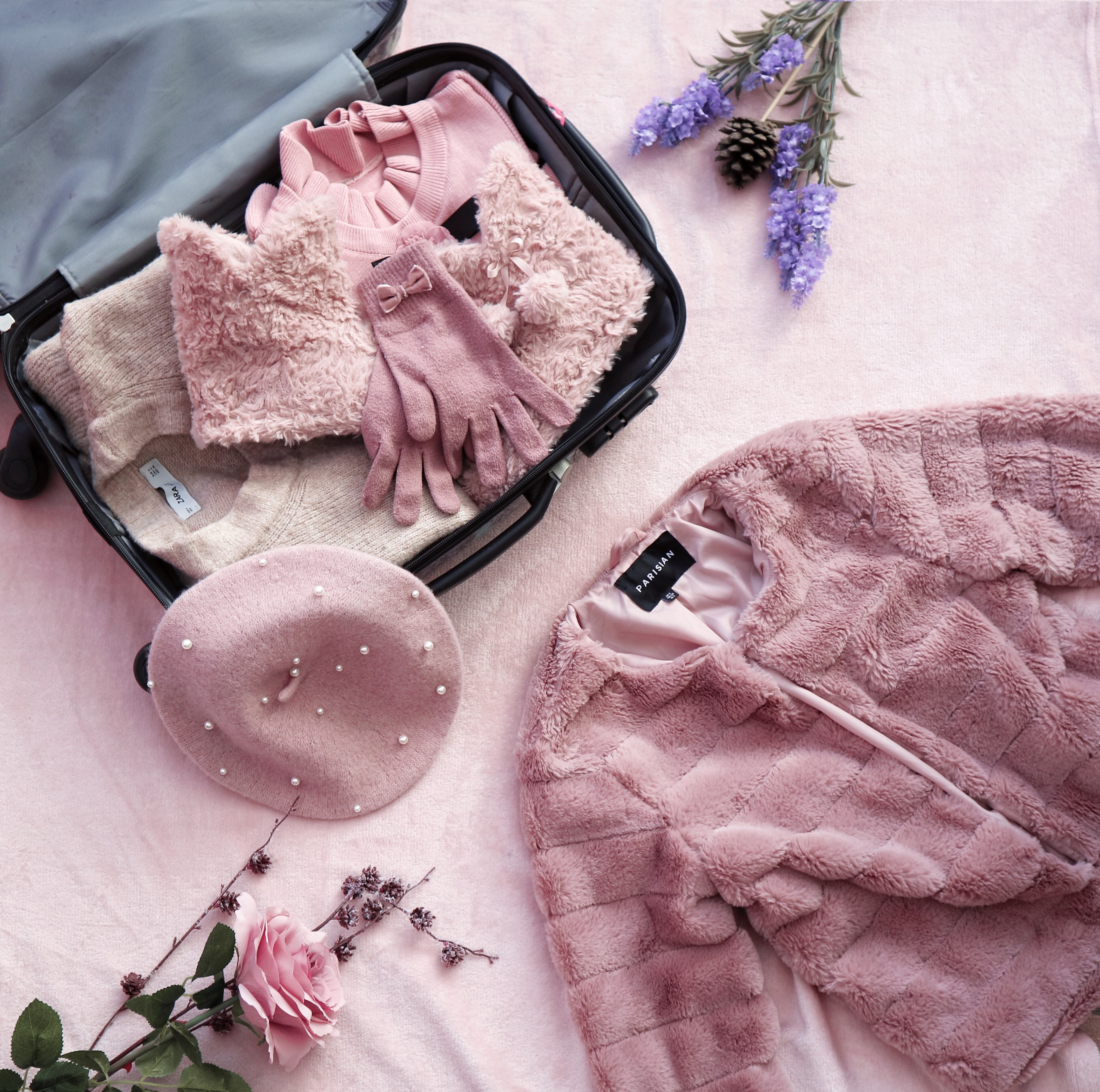 What to pack for a winter getaway:

A suitcase full of pink clothes is lying on a pink floor surrounded by springtime flowers and a pink faux fur coat.
