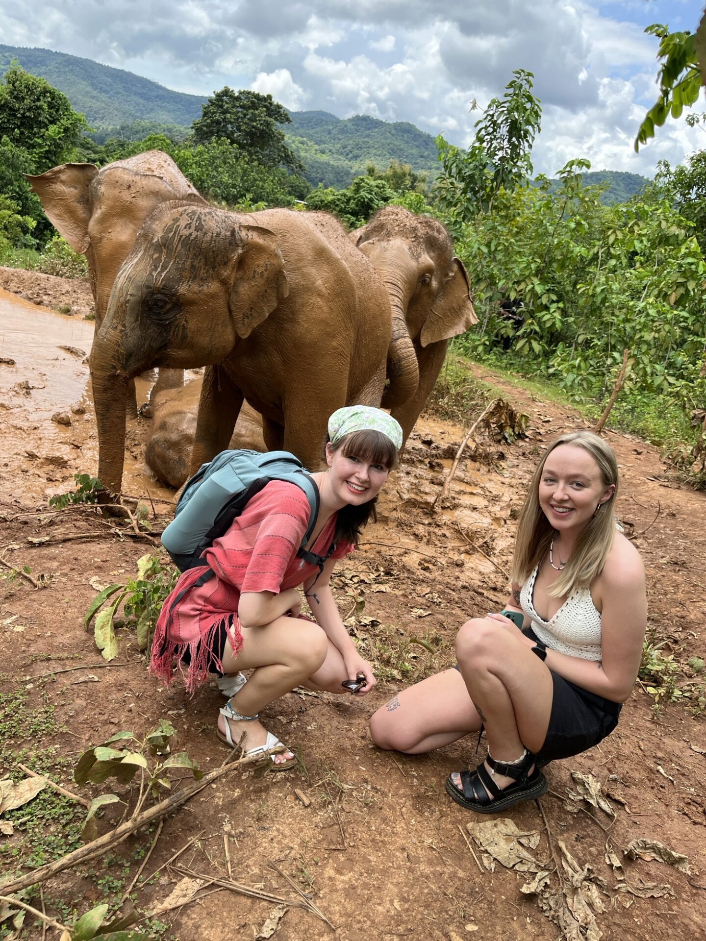 Chloe and Elicia crouched in front of a herd of elephants.
